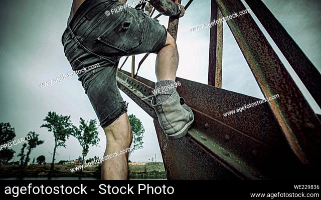 Man with tattooed body climbs on an old rustic crane and walks toward end to sit