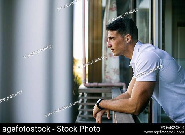 Man looking away while leaning on railing at balcony