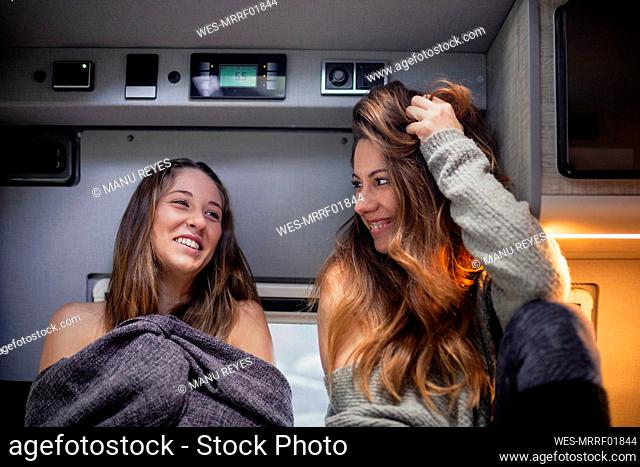 Smiling woman with hand in hair by friend at camper van
