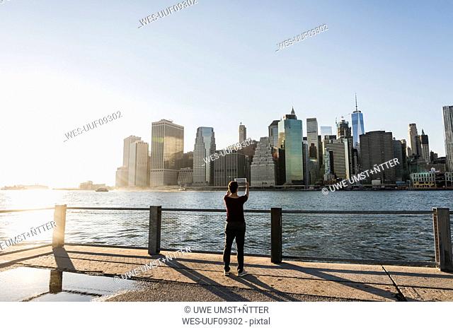 USA, Brooklyn, back view of woman taking picture of Manhattan skyline with tablet