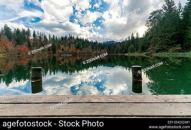 wooden pier and boardwalk with dock pylons on the edge of an idyllic mountain lake surrounded by fall color forest in the Alps of Switzerland near Flims in the...
