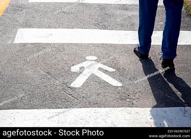 Pedestrian sign on the asphalt and human legs walking on sunny day