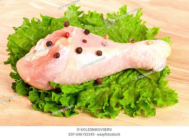 one raw chicken drumsticks with lettuce leaf on a wooden cutting board on white background