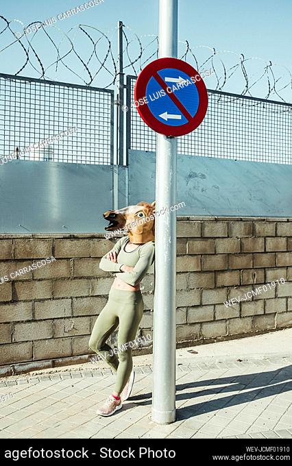 Woman in horse mask leaning on pole