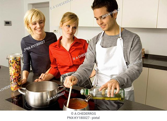 Two young women and a young man preparing food in the kitchen
