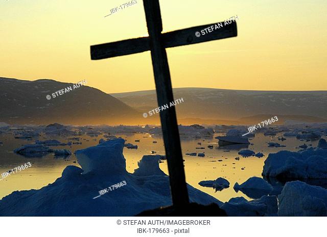 Cross in front of sunset over icebergs Paarnakajiit Sermilik Fjord Eastgreenland