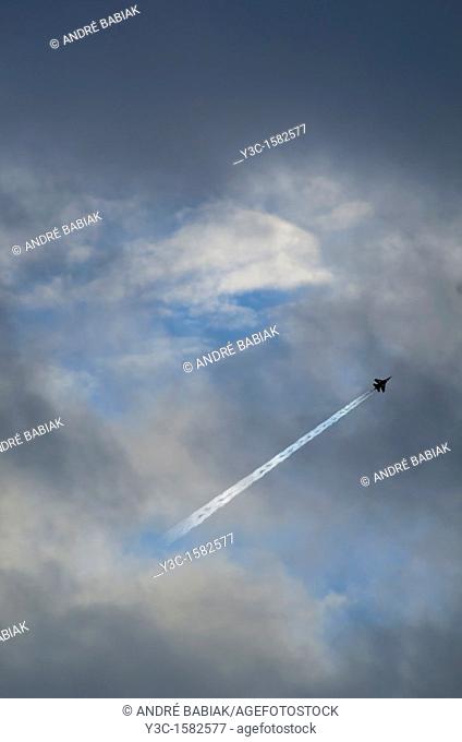 Military jet fighter aircraft leaving condensation trail in cloudy sky
