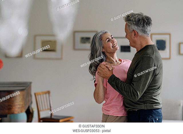 Happy senior couple dancing in living room at home