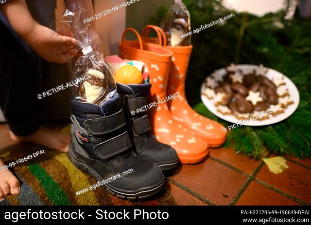 06 December 2023, Lower Saxony, Hanover: Children's boots filled with chocolate Santa Clauses, mandarins and other items stand outside the front door of a...