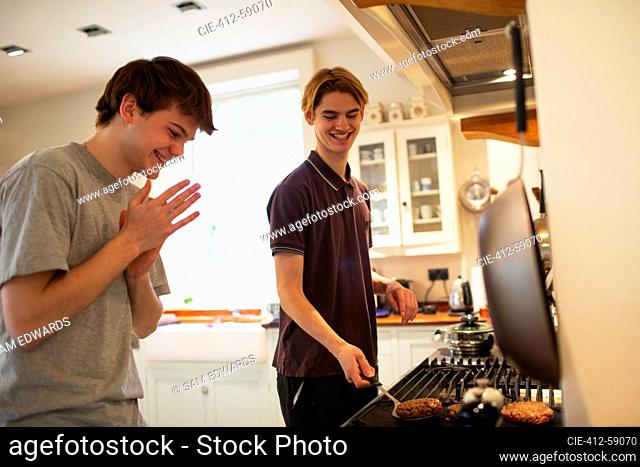 Happy teenage boys grilling hamburgers at kitchen stove