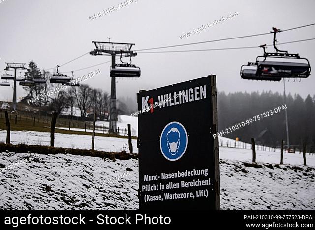 09 March 2021, Hessen, Willingen: A notice board with the inscription ""Mund-Nasenbedeckung. Mandatory in all areas!"" is located in front of the chairlift...