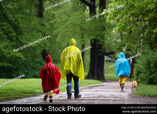 13 May 2021, Saxony, Leipzig: Strollers walk in colorful raincoats through the Clara Zetkin Park in Leipzig. Ascension Day turns out to be rainy in many places...