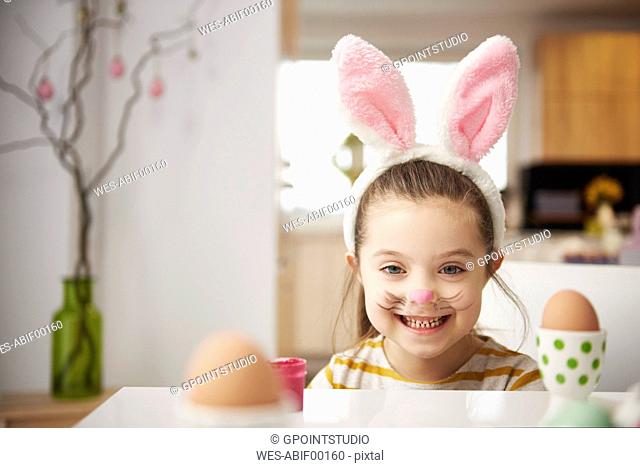 Portrait of smiling girl with bunny ears sitting at table with Easter eggs