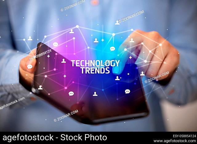Businessman holding a foldable smartphone with TECHNOLOGY TRENDS inscription, new technology concept