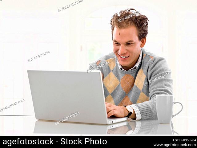 Happy young man working on laptop computer at home, smiling