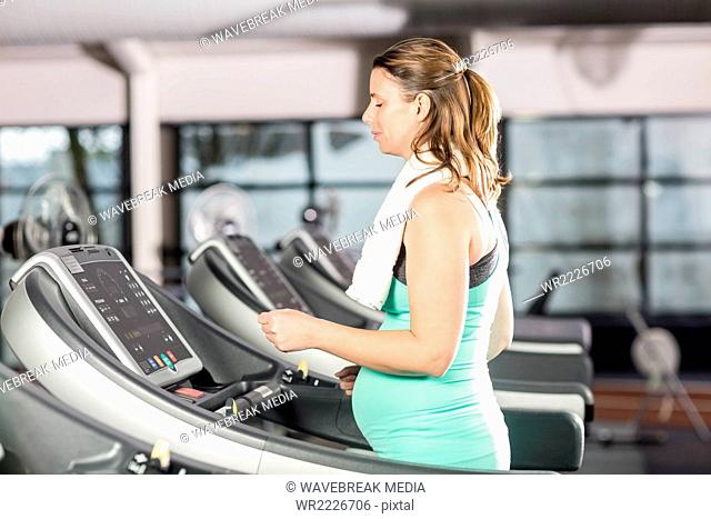 Smiling pregnant woman using treadmill