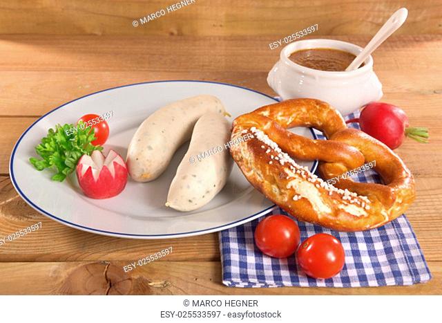 weißwurstfrühstück with two sausages, pretzels and sweet mustard on wooden boards\n