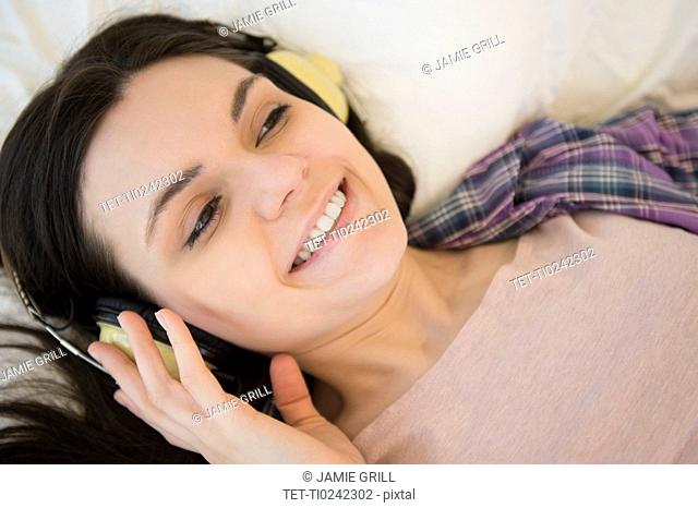 Portrait of young woman lying down on bed and listening to music