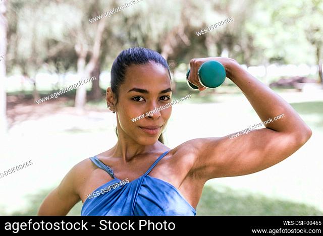 Young female athlete with dumbbell exercising at park