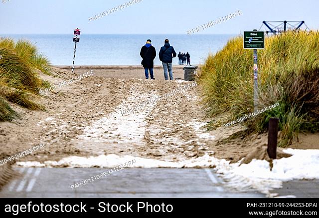 10 December 2023, Mecklenburg-Western Pomerania, Warnemünde: Beachgoers walk along Warnemünde beach in temperatures just above freezing and light drizzle...