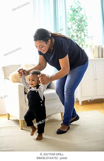 Mixed race mother helping baby son walk in living room