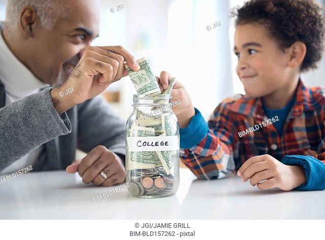 Mixed race grandfather and grandson saving money in college fund jar