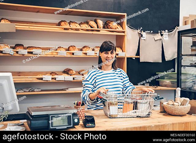 Smiling store owner with shopping basket at checkout counter