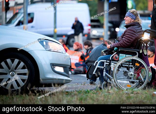 23 October 2023, Berlin: A woman in a wheelchair is seen in front of a car crossing the sidewalk during a road blockade by the climate protection group ""Last...