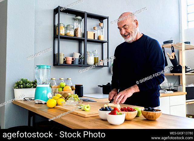 Senior man cutting banana on cutting board in kitchen