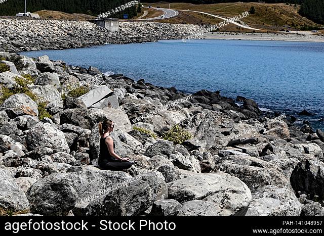 Lake Pukaki; a woman meditates on a stone on the bank; Stone bank; on January 5th, 2019 near Twizel in the Canterbury region on the South Island / New Zealand;...