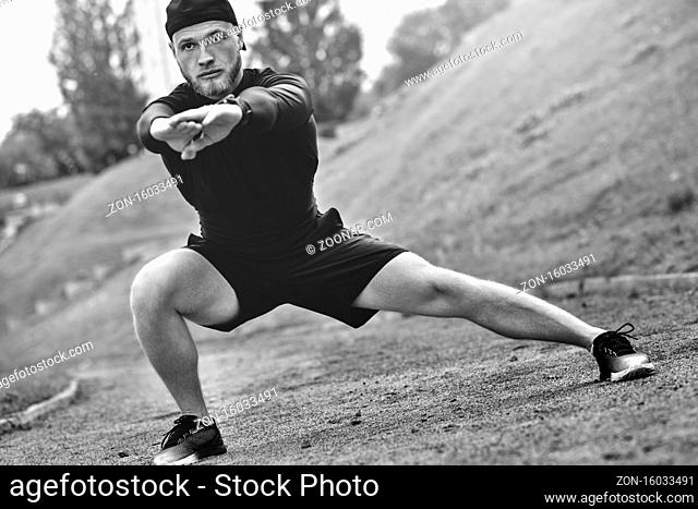 Muscular sportsman stretching out before a sports training at the street in city park