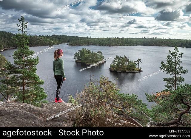 Woman while hiking looks out over small islands in Lake StensjÃ¶n in Tyresta National Park in Sweden