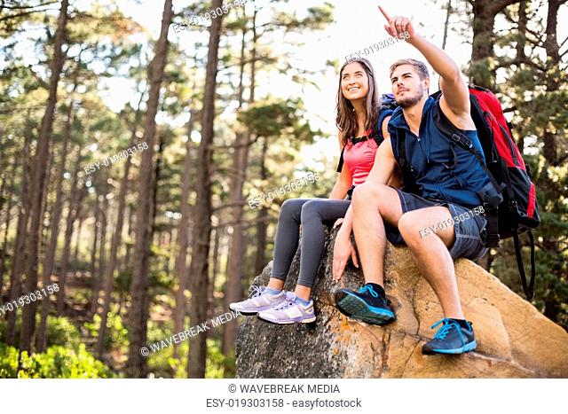 Young happy joggers sitting on rock feeling and pointing at something
