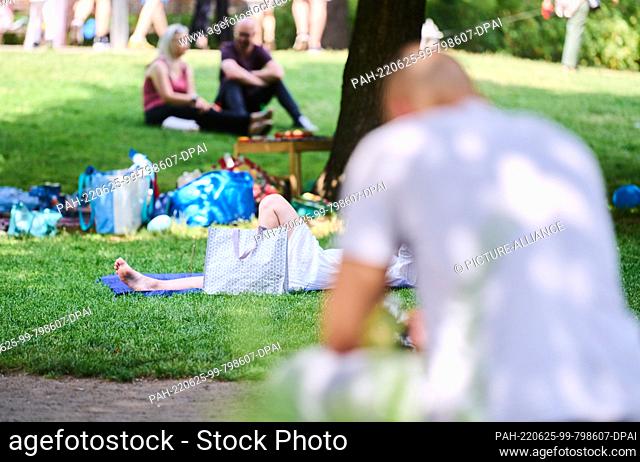25 June 2022, Berlin: People lie and sit in the shade of the trees in the Volkspark am Weinberg in Mitte. There is sultry heat in Berlin at the weekend