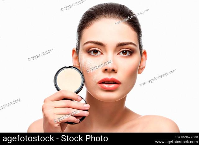 Beautiful young woman holding conrainer with pressed powder next to her face. Isolated over white background