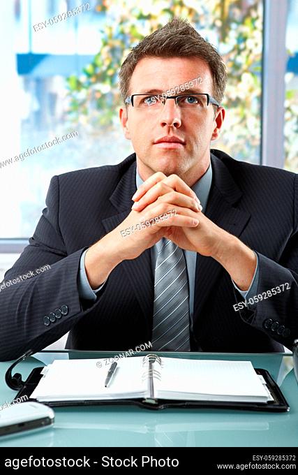 Successful executive businessman wearing suit and glasses looking at camera with hands folded