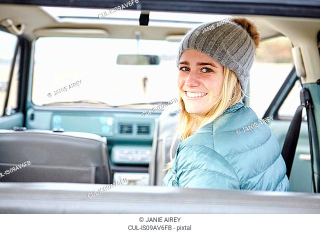 Portrait of young woman in car at beach wearing knit hat