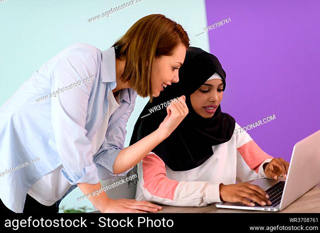 afro muslim woman wearing a hijab sits smiling in her home office and using laptop for online meeting