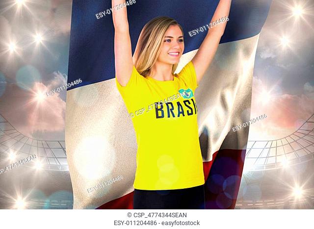 Excited football fan in brasil tshirt holding france flag against large football stadium under cloudy blue sky