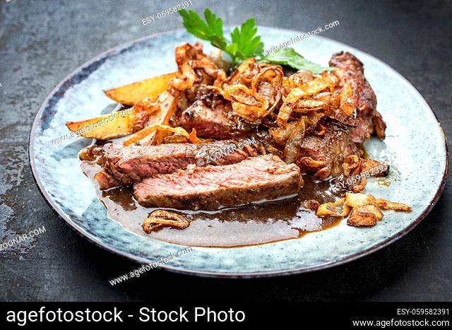 Traditional dry aged sliced roast beef with fried onion rings and potato chips as closeup on a plate with brown sauce