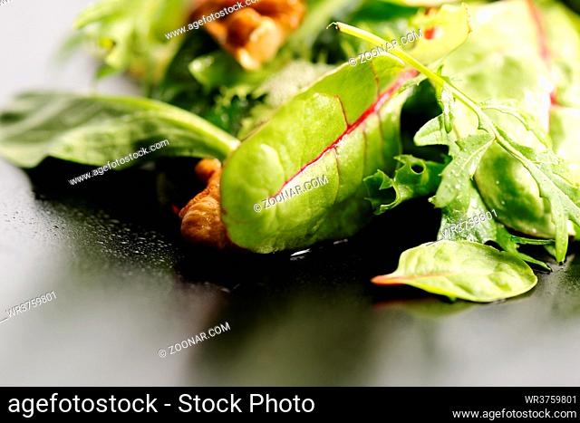 Fresh ecological salad mix with nuts on black plate, macro