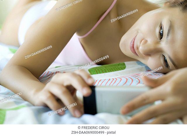 Smiling young woman lying on bed looking at cell phone