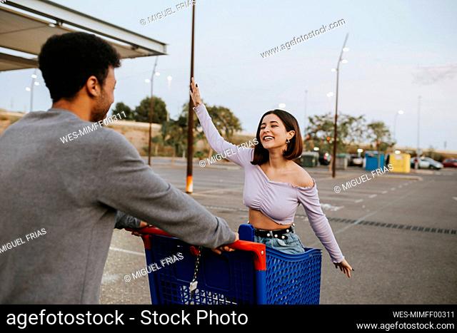 Carefree woman sitting in shopping cart by man