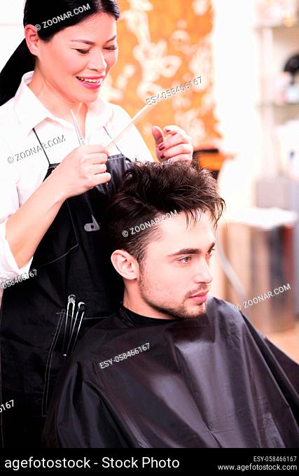 Beautiful young hairdresser working in hairdressing salon and making haircut for handsome man. Handsome man looking at mirror