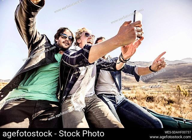 Happy friends in convertible car on a road trip taking a selfie