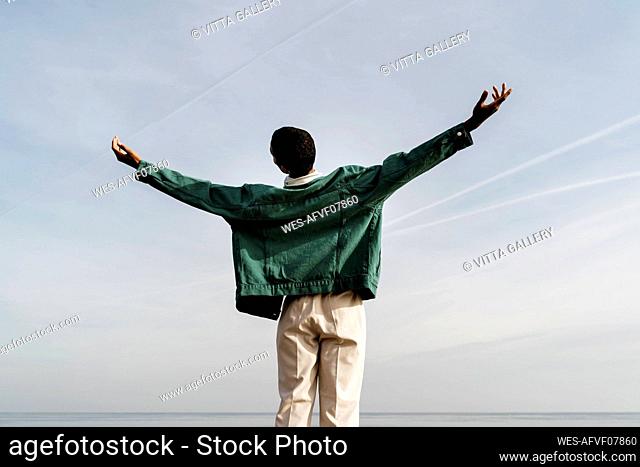 Young man with arms outstretched against sky