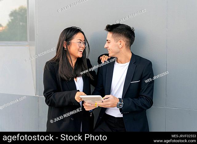 Businessman with tablet PC looking at colleague in front of gray wall
