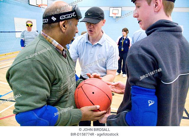 Coach talking to Team members who are holding a ball during a Goalball training, a threeaside game developed for the visually impaired and played on a...