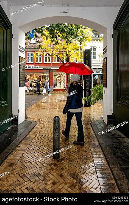 Odense, Denmark A woman with a red umbrella walks through an old brick alley in the rain on Vestergade in downtwon