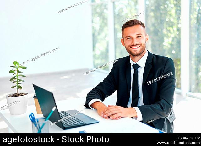Stylish smiling businessman in elegant suit sitting at his desk in a bright modern office. business success concept